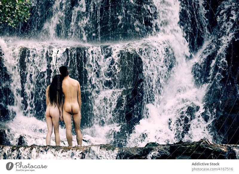 Unrecognizable naked couple near waterfall nude nature enjoy scenery calm close relationship summer together body rock romantic love sensual boyfriend