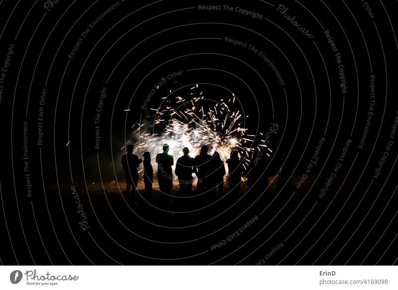 Group of People in Silhouette Watch Fireworks Close Up on Beach fireworks beach night light explosion glow colorful explode celebration party New Yearâ€™s Eve