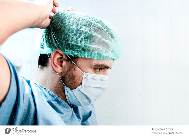 Medical specialist putting on mask before treatment of patient medic surgeon put on prepare sterile man medical protect hospital serious professional male cap