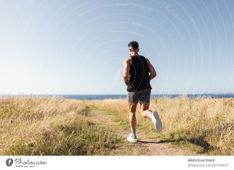 Man running along path at seaside runner man summer jogger training cardio endurance sunny male athlete meadow exercise healthy muscular energy wellbeing