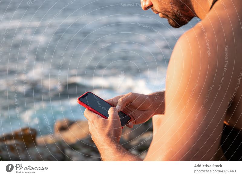 Man sitting on seashore and browsing smartphone man social media surfing relax entertain sunset male summer rock using gadget device communicate online internet