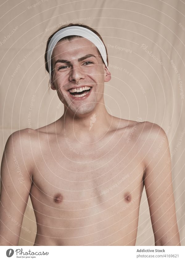 Young shirtless androgynous man laughing makeup appearance transgender happy model young male headband piercing excited queer lgbtq fashion joy positive style