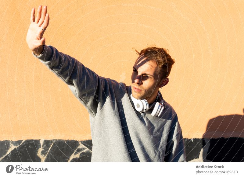 Young man with headphones covering face from sunlight sunshine protect outstretch hipster urban male modern unshaven casual wall street lifestyle street style