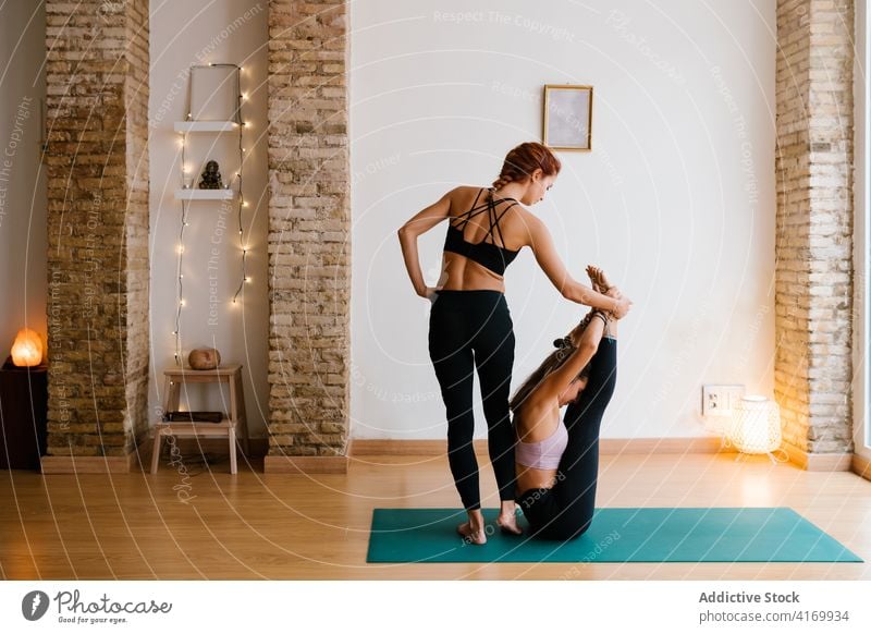 Instructor helping woman to do Urdhva Mukha Pascimottanasana pose women instructor yoga studio stretch practice bend support boat with thighs to chest pose slim