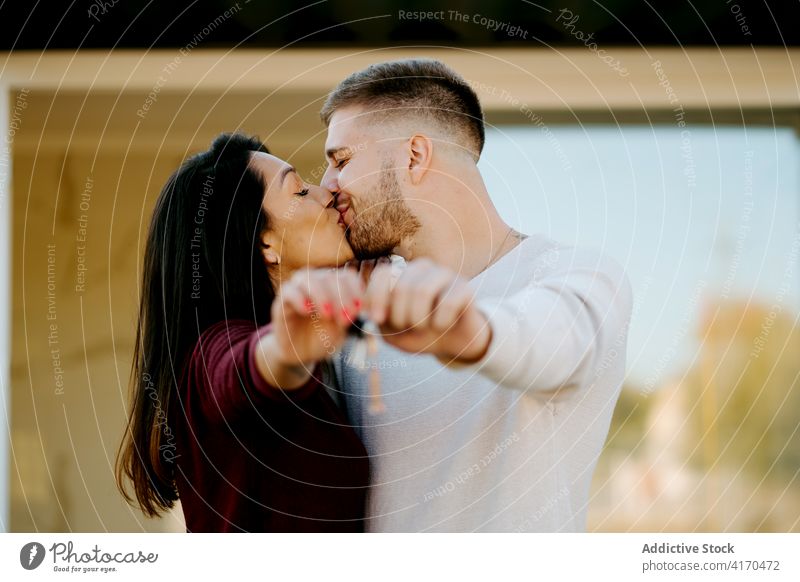 Excited couple with keys from new house real estate kissing excited hug homeowner together embrace smile cheerful relationship property enjoy happy positive