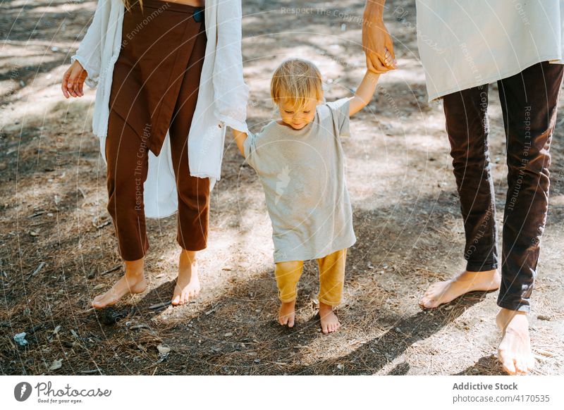 Anonymous couple walking with kid in forest hippie family child barefoot nature enjoy unity multiethnic multiracial diverse woods sunny cute toddler love