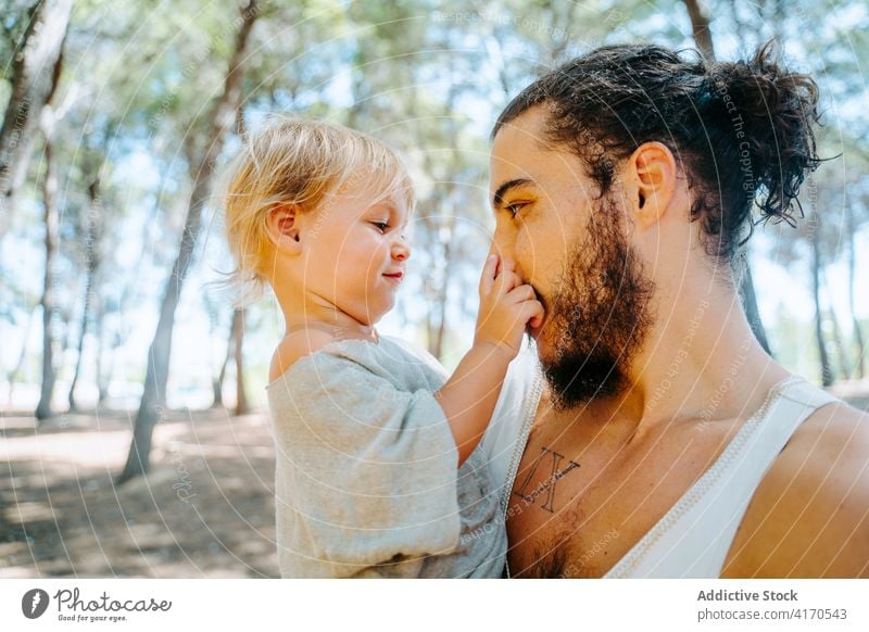 Happy father cuddling cute kid in forest kiss child cheek love tender together weekend ethnic multiracial diverse parenthood fatherhood adorable hipster enjoy