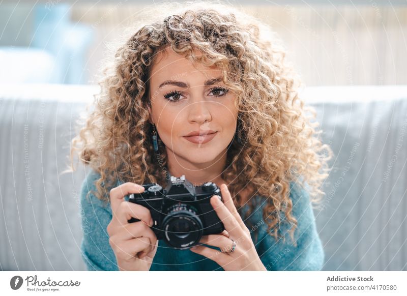 Cheerful woman with photo camera at home photographer take photo cheerful talent cozy photography curly hair female bright apartment casual charming gadget