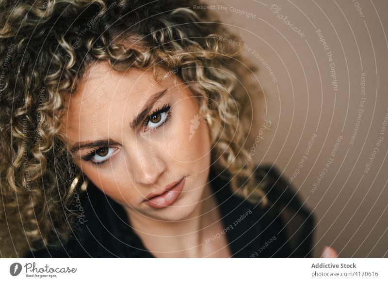 Stylish woman posing at studio looking at camera close up sit curly hair elegant outfit afro thoughtful style trendy female fashion calm concentrate beauty