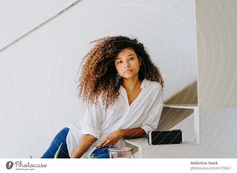Stylish ethnic woman with curly hair sitting on steps at home style afro trendy stair calm relax modern attractive young female hairstyle long hair lifestyle