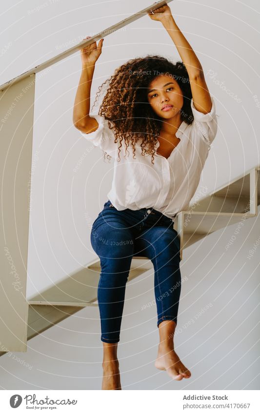 Ethnic curly haired woman sitting on stairway style trendy hairstyle afro barefoot modern attractive young ethnic female long hair fashion lifestyle brunette