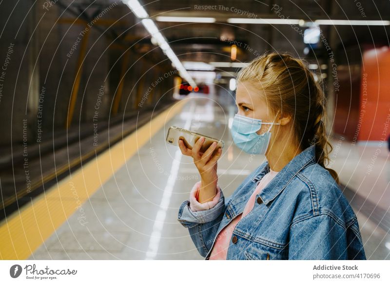 Woman in mask recording audio message on smartphone at train station woman passenger using cellphone coronavirus voice railway journey female covid covid19