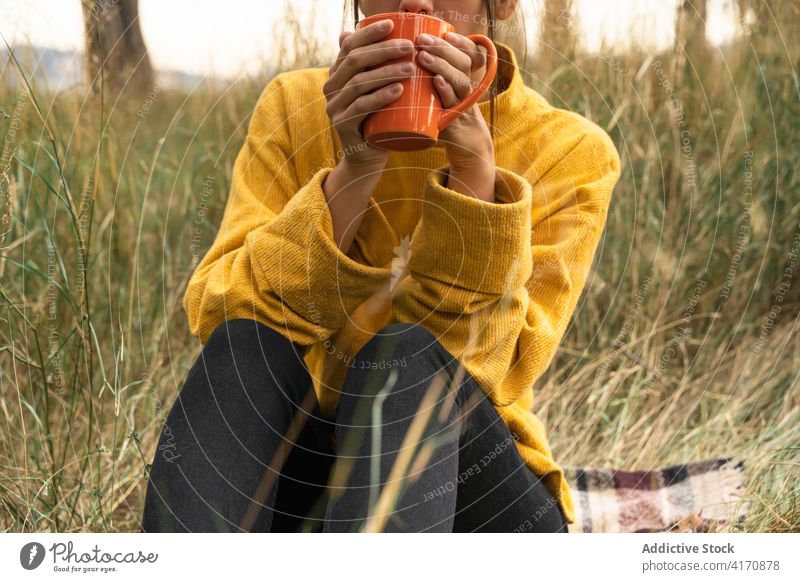 Anonymous woman enjoying fresh tea in countryside hot drink field autumn nature carefree fall female beverage weekend serene relax rest casual mug season lady
