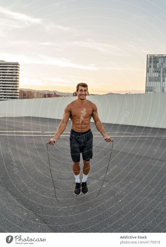 Happy sportsman jumping rope on road in twilight athlete cardio workout exercise training smile street city happy content muscular shirtless town fit