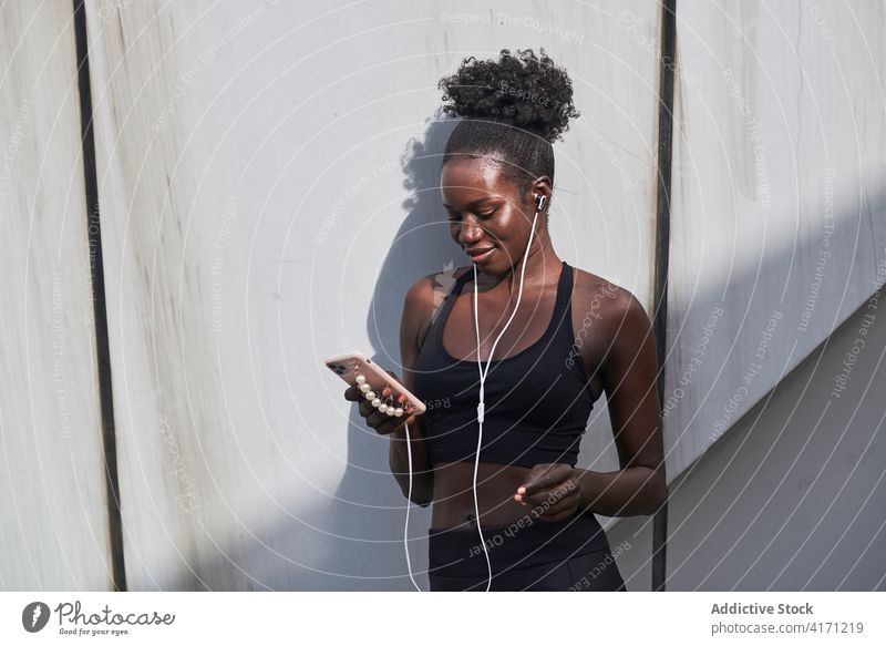 Happy thnic sportswoman listening to music on smartphone earphones athlete street city workout fit female ethnic black african american sunny sportswear urban