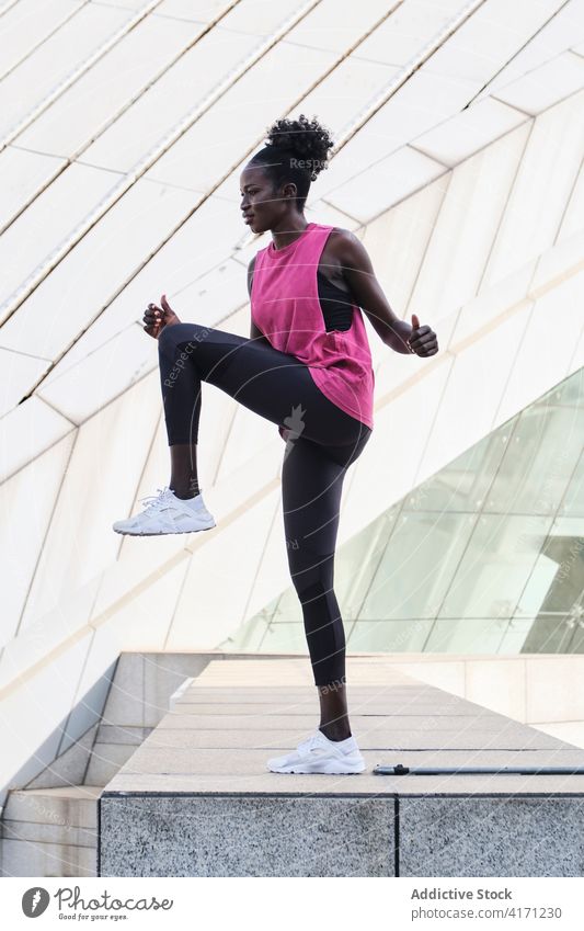Ethnic sportswoman warming up legs during training warm up city athlete active stretch workout fit female ethnic black african american slim sportswear wellness