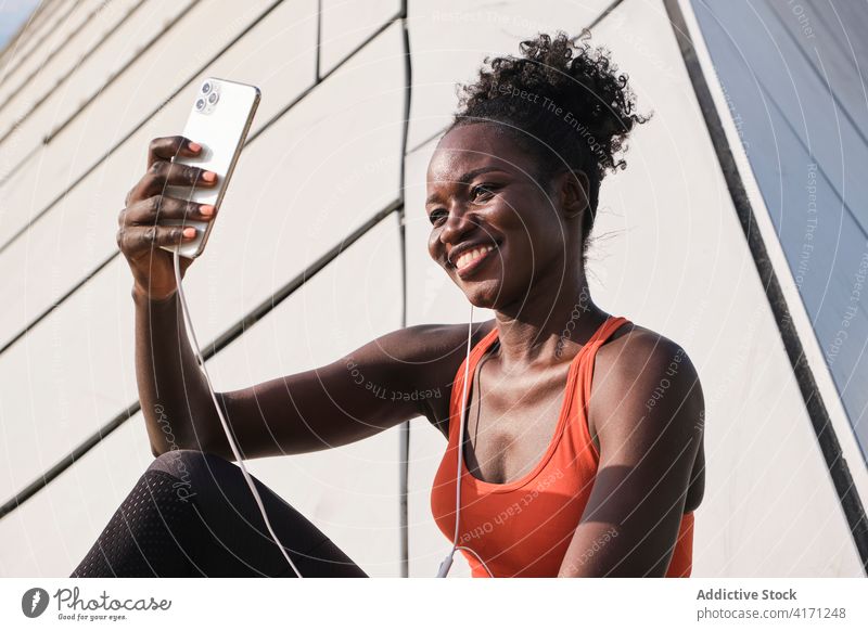 Ethnic sportswoman listening to music in earphones smartphone selfie athlete street song cheerful relax self portrait female taking ethnic black photo