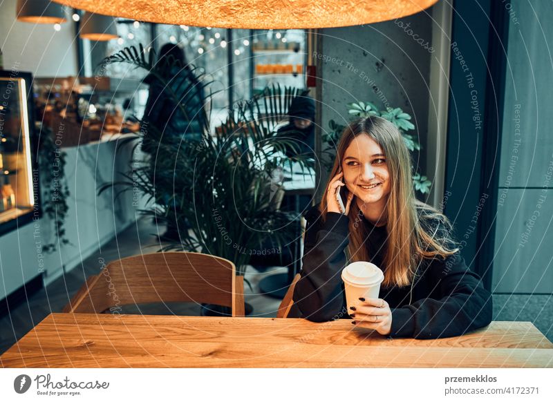 Young woman talking on the phone at cafe, having a pleasant phone call, answering call, chatting by mobile phone with friend while sitting in a cafe and drinking coffee. Girl relaxing in cafe