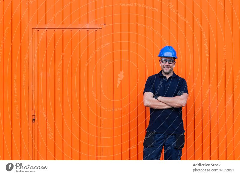 Cheerful male worker in hardhat standing near workshop cheerful confident friendly man professional mechanic positive wall adult workman bright smile job happy