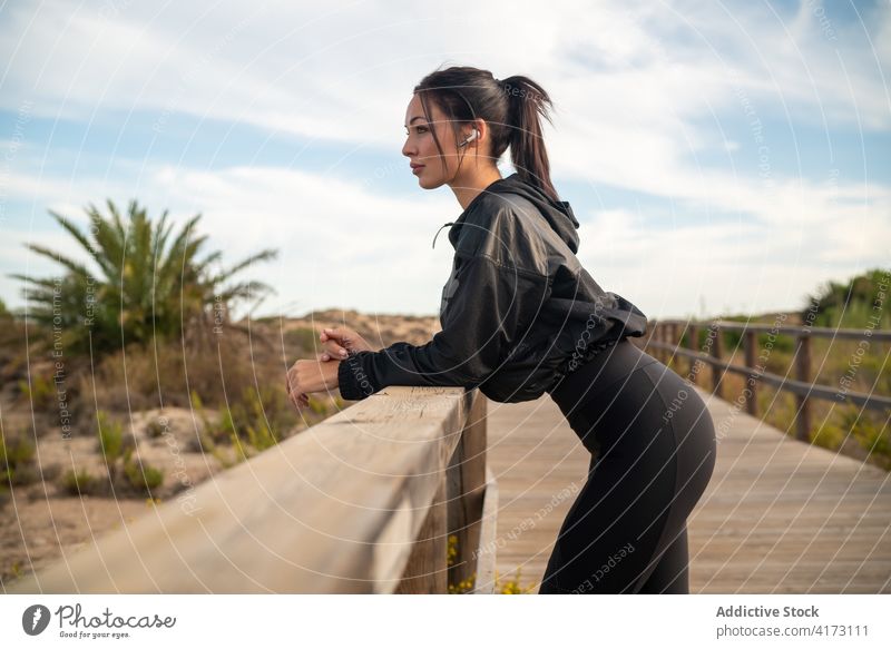 Fit sporty woman resting after training on boardwalk fit relax fitness workout earphones recreation recovery listen active exercise nature young lifestyle