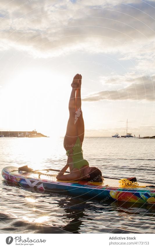 Woman practicing balancing yoga pose on paddle board woman salamba sarvangasana inversion balance sea sunset sup board supported shoulder stand water slim