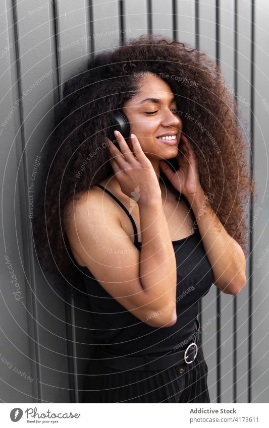 Charming ethnic woman with headphones on street curly hair afro hairstyle charming smile natural beauty female listen black african american city trendy rest