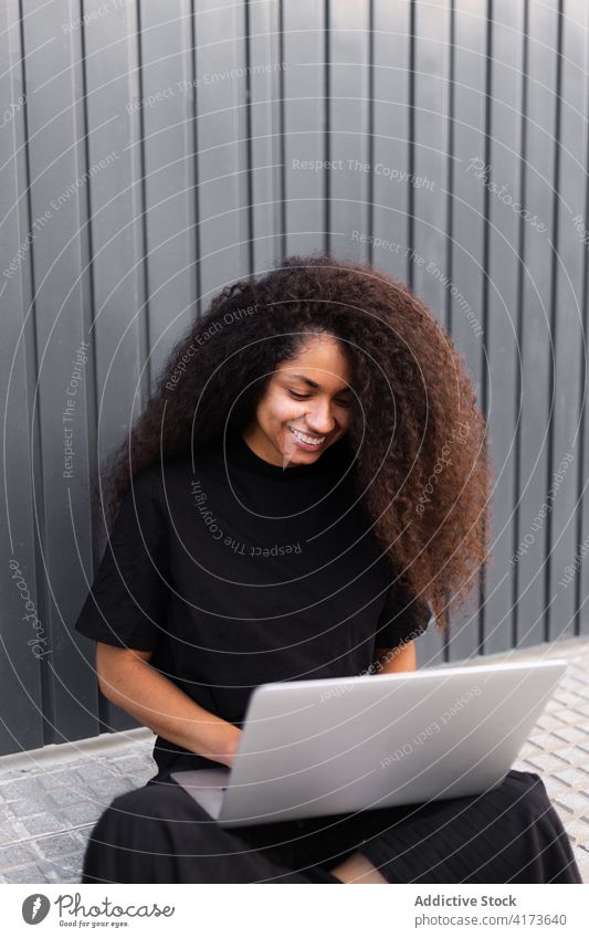 Cheerful African American self employed woman sitting on street with laptop freelance curly hair city entrepreneur ethnic black african american cheerful