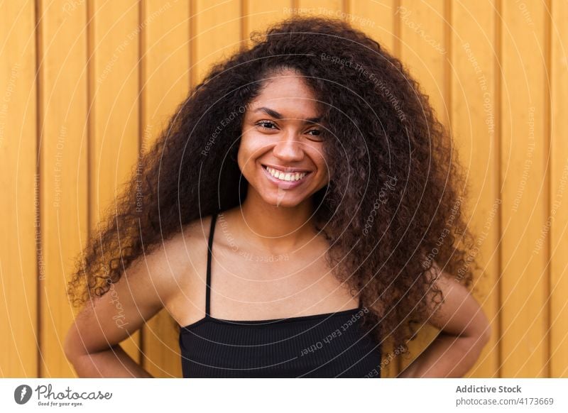 Cheerful black woman with curly hair in street afro hairstyle smile portrait sincere candid young female ethnic african american delight joy wooden wall relax