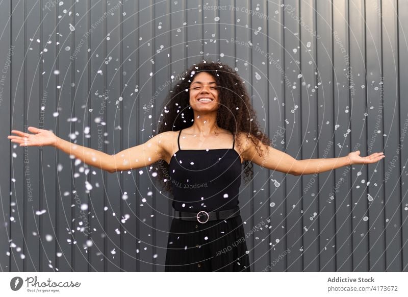 Black woman scattering confetti on street toss having fun cheerful delight festive celebrate event female ethnic black african american city happy smile