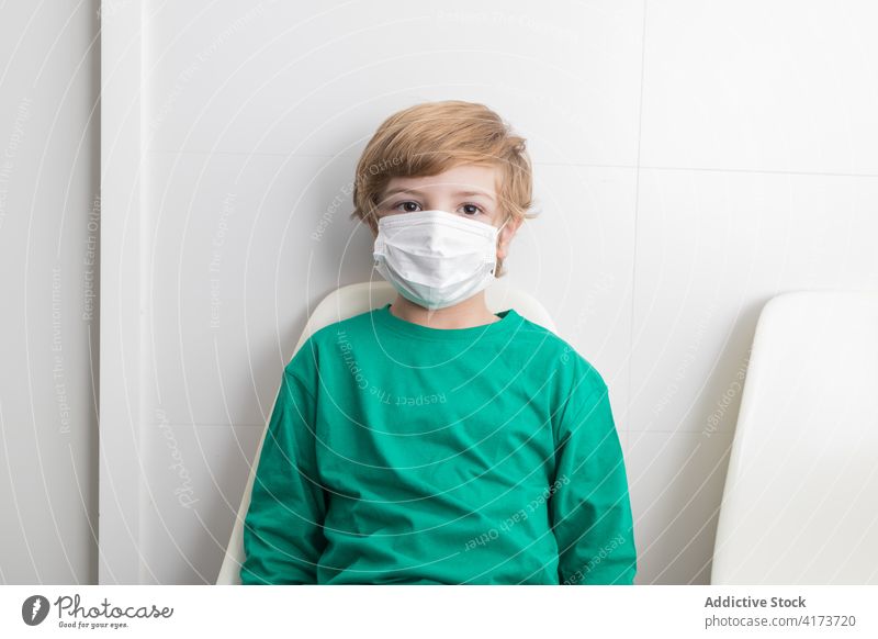 Child wearing medical mask in hospital child coronavirus kid covid 19 boy protect clinic chair room sit calm covid19 epidemic prevent outbreak pandemic