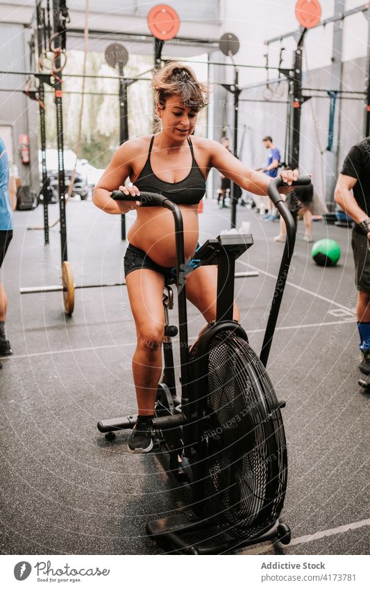 Pregnant woman doing exercises on air bike in sports center pregnant sportswoman gym cycle machine cardio functional training female athlete physical wellbeing