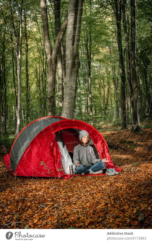 Woman meditating near tent in forest - a Royalty Free Stock Photo