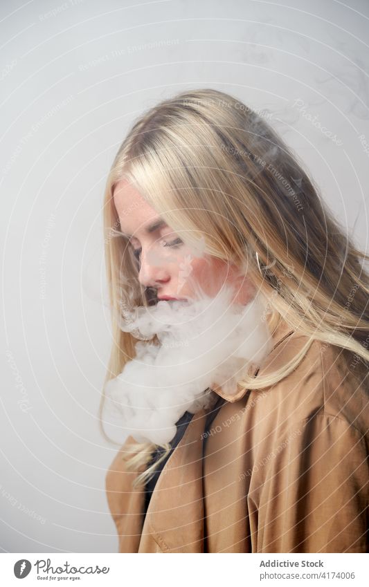Young woman smoking e cigarette in studio vape smoke steam style cool nicotine smoker female habit confident young bad unhealthy serious addict trendy lady fume
