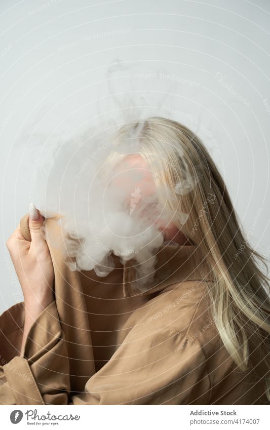 Anonymous woman covered by smoke in studio e cigarette vape steam style cool nicotine smoker female habit confident bad unhealthy addict trendy blonde lady fume
