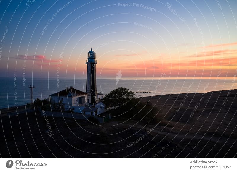Lonely lighthouse on coast of sea at sunset beacon navigate tower sky twilight landscape amazing calm hill ocean picturesque shore sundown peaceful scenic