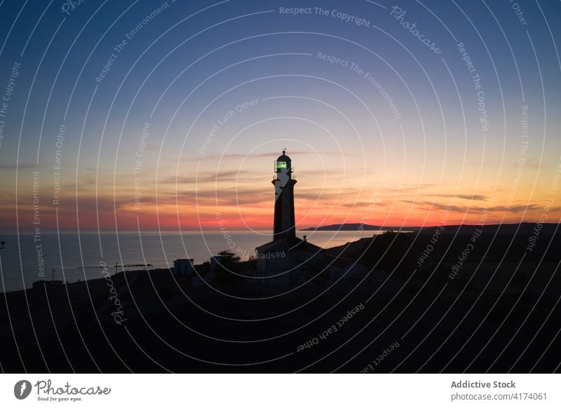 Lonely lighthouse on coast of sea at sunset beacon navigate tower sky twilight landscape amazing calm hill ocean picturesque shore sundown peaceful scenic