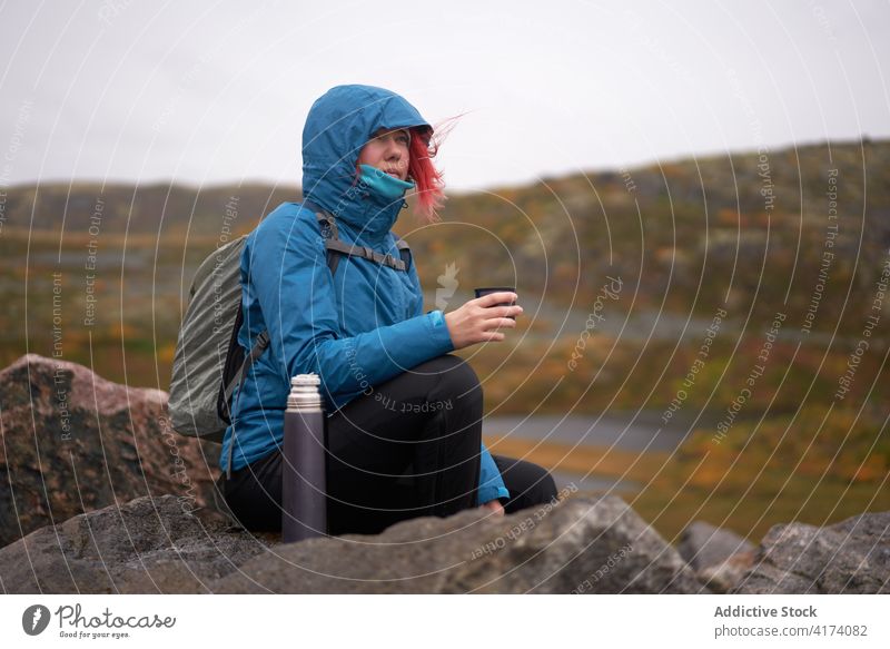 Female explorer drinking tea from thermos cup in highlands traveler woman mountain hot autumn gloomy adventure female wanderlust landscape rock outerwear