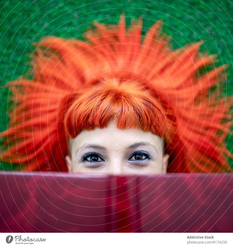 Woman with red hair and book resting on lawn woman read ginger vivid peek park colorful bright female adult grass redhead rebel dyed hair subculture alternative
