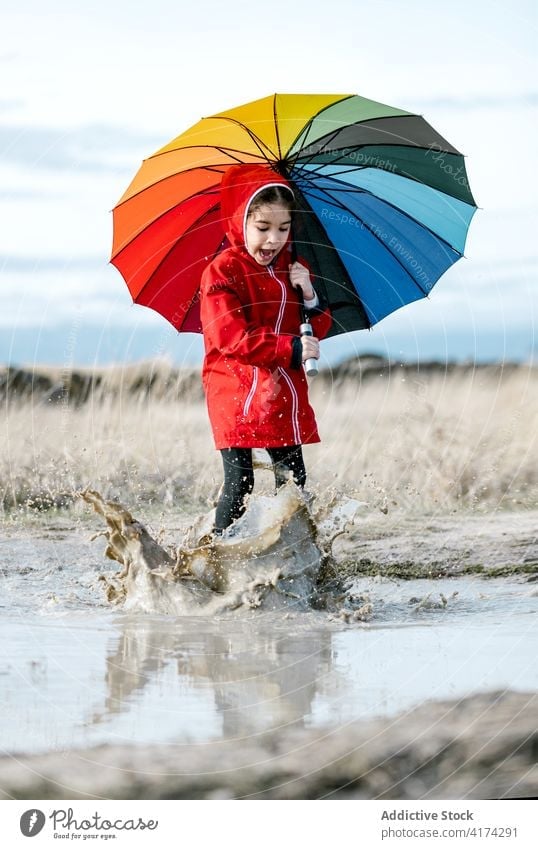 Cheerful girl with umbrella playing in puddle splash water child together childhood raincoat having fun playful rubber boot kid joy happy laugh cheerful weekend