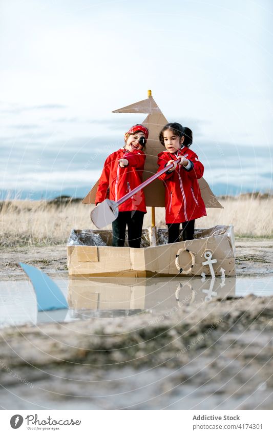 Excited girls playing in cardboard boat in countryside having fun carton child together inspiration paddle game creative imagination handmade cheerful happy