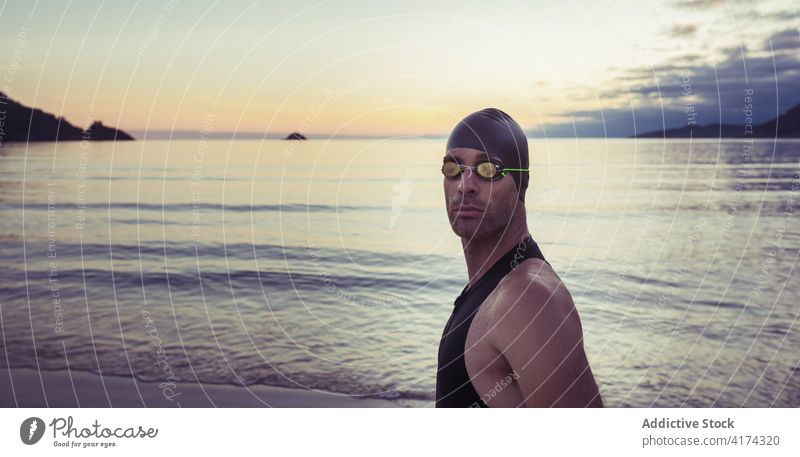 Male swimmer in goggles at seaside man seashore professional sportsman swimsuit cap beach male confident coast ocean stand water summer sunset sky nature guy