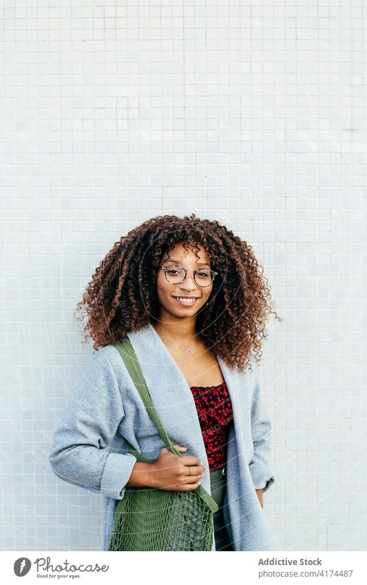 African American woman near tiled wall lean street rest style smile city outfit casual female bag cotton trendy happy curly hair black ethnic african american