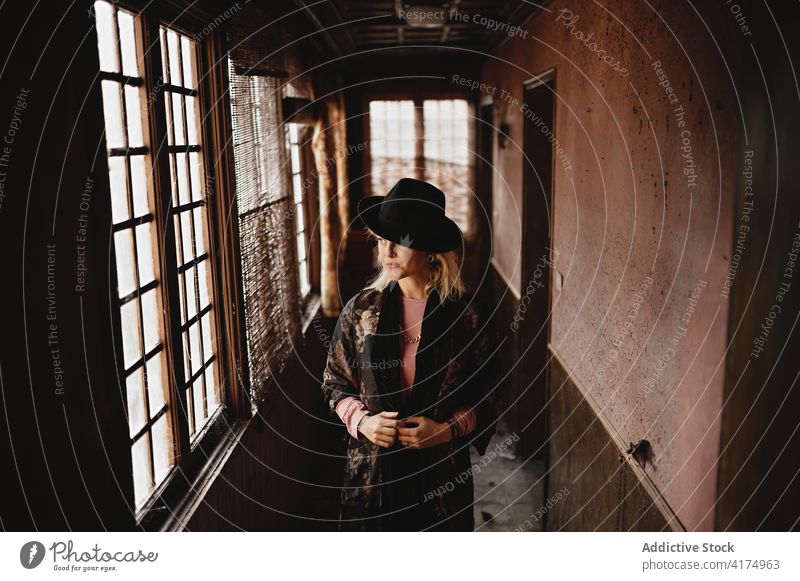 Woman in hat standing in corridor of old house woman vintage window style old fashioned elegant female hallway retro pensive thoughtful abandoned art aged lady