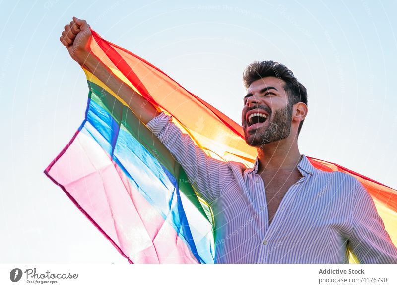 Optimistic gay man with LGBT flag in city lgbt homosexual rainbow street expressive scream lgbtq male pride tolerance cheerful right equal freedom gender smile