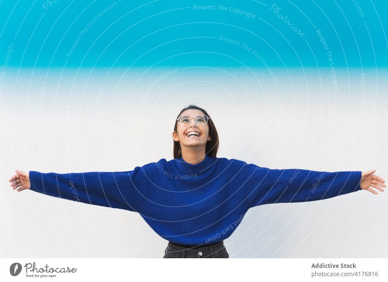 Excited woman with outstretched arms in city millennial cheerful enjoy freedom carefree weekend female light filter blue trendy delight glad street smile young