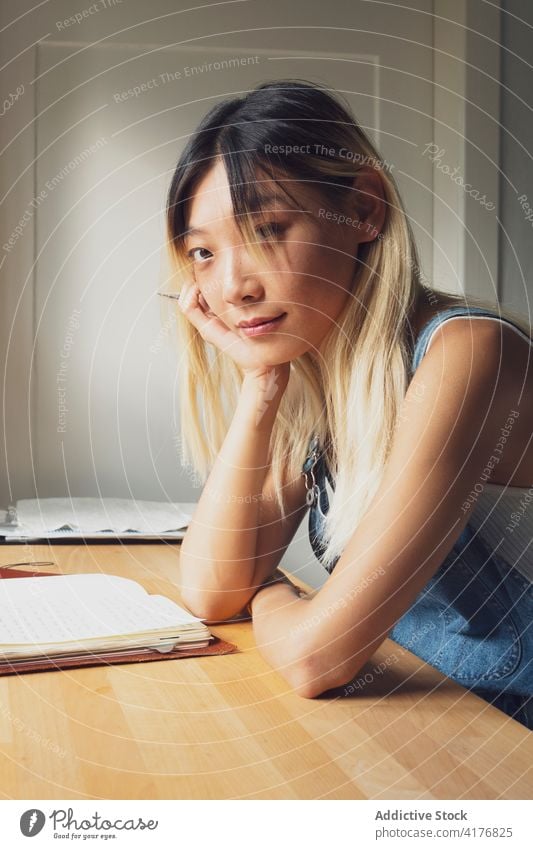 Ethnic woman taking notes in notebook at home take note thoughtful diary lean on hand think notepad table female asian ethnic pensive relax casual content style