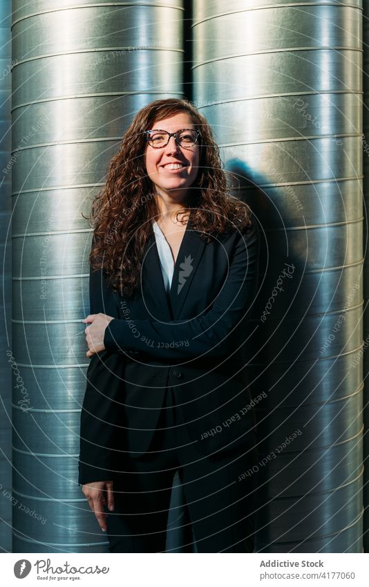 Cheerful businesswoman in suit in warehouse cheerful confident storehouse facility plant modern metal determine barrel glad female optimist formal entrepreneur