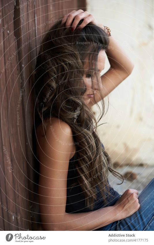 Tranquil woman with long hair near old building touch hair tranquil carefree calm appearance wavy hair female weathered young harmony style trendy daytime