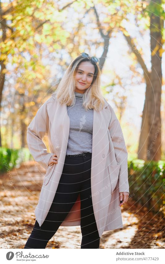 Young woman in coat in autumn park outfit smile stroll weekend casual young female cheerful happy optimist hand on waist delight trendy pleasant glad positive