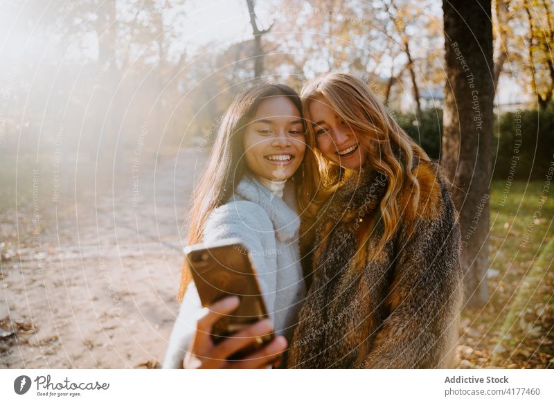 Friendly women taking selfie in autumn park friend smartphone cheerful self portrait memory stroll female multiracial multiethnic diverse photo warm coat